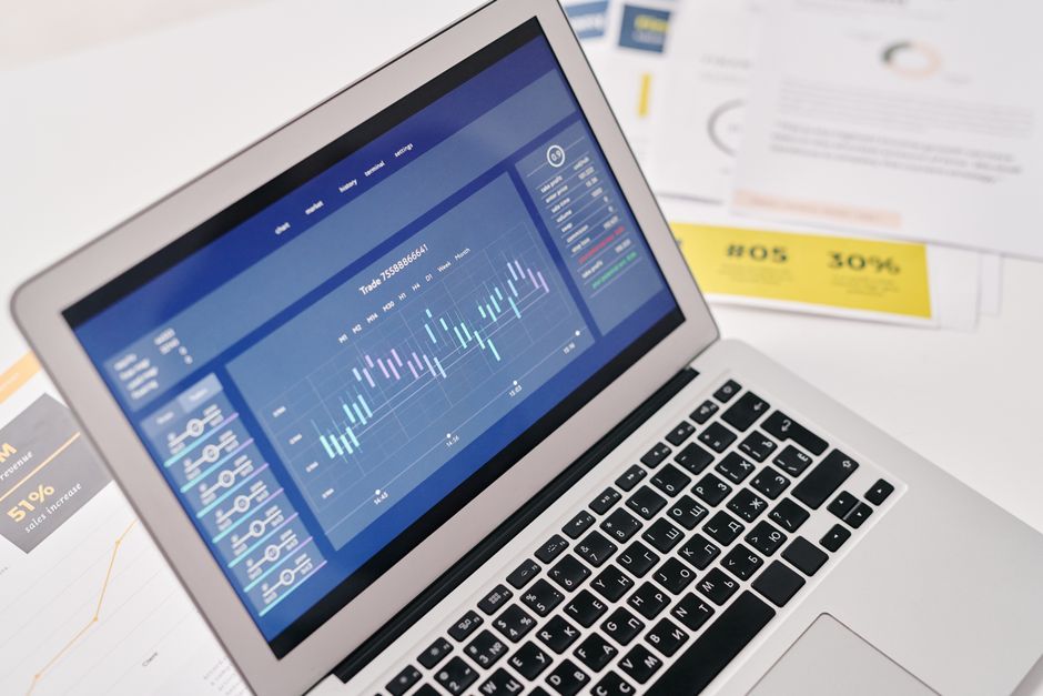 Otvoreni laptop s financijskim grafovima i analitikom te dokumentima za poslovnu prezentaciju